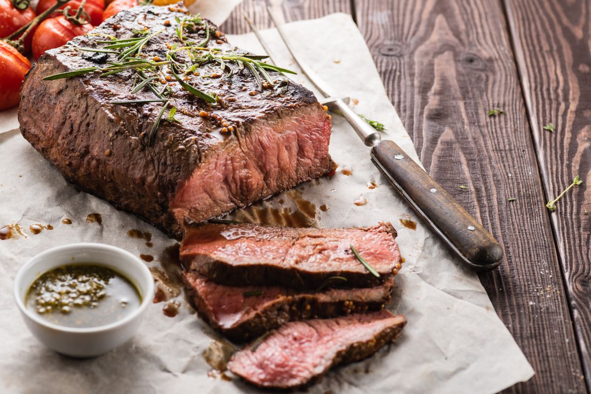 A succulent bottom round roast, perfectly browned and resting on a wooden carving board, surrounded by an array of fresh herbs and spices, with a carving knife and fork set to the side, ready for serving